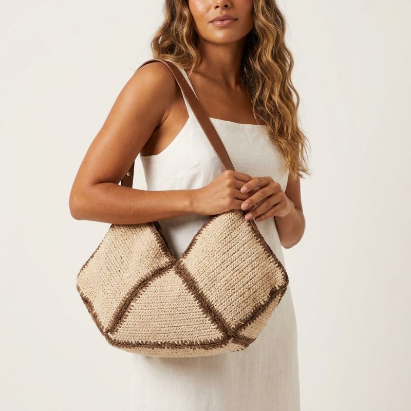 Mulher de vestido branco carregando a bolsa de praia de palha Lívia no ombro