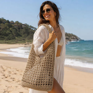 Mulher com bolsa de praia em crochê bege no ombro em praia com mar ao fundo