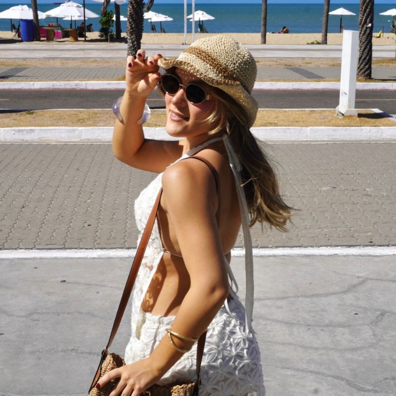 Mulher usando chapéu de palha aba ondulada caminhando à beira-mar em dia ensolarado